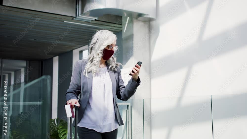 Senior woman with face masks walking through airport gate, looking on smartphone. Coronavirus concept. Senior woman with face masks walking through airport gate, looking on smartphone. Coronavirus concept.