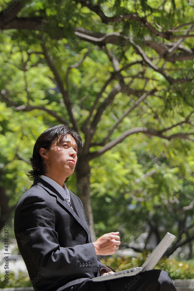 A young Japanese businessman thinking while using a personal computer in a business district in Los Angeles, USA A young Japanese businessman thinking while using a personal computer in a business district in Los Angeles, USA
