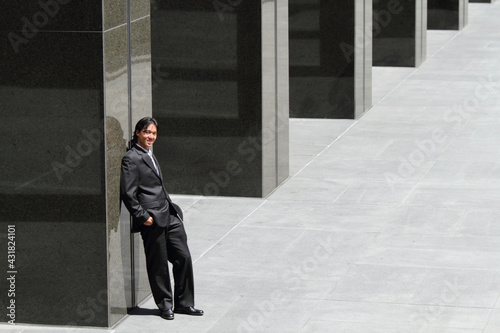 A young Japanese businessman leaning against a building in a business district in Los Angeles, USA 