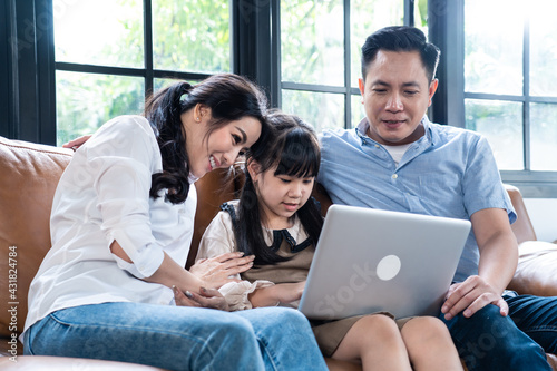 Asian family teaching their daughter to use laptop computer at home.