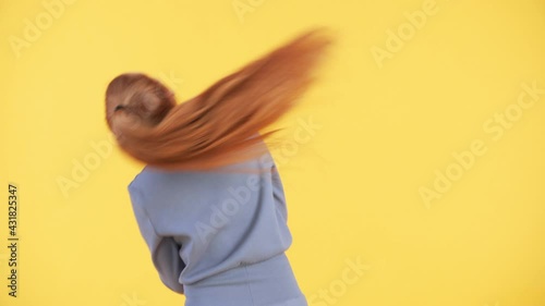 Back of a woman with long ginger ponytail dancing and moving her hair. Yellow background. Woman is dancing enjoying herself