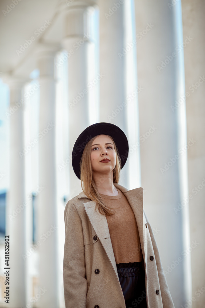 a young girl in a hat and glasses stands against the background of a building with columns