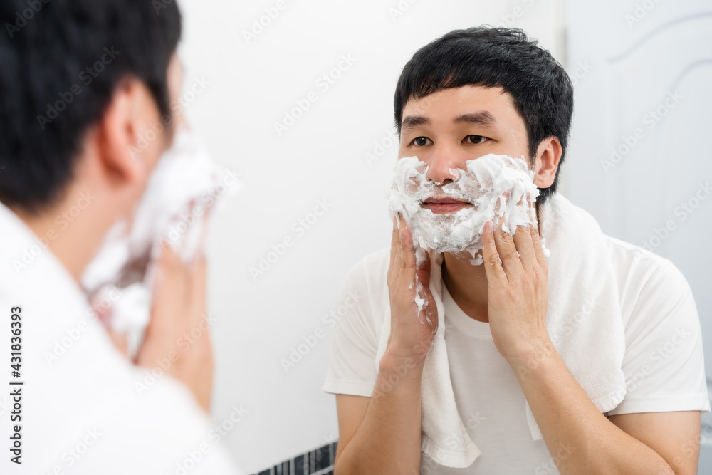 man applying foam cream on face before shaving in the bathroom mirror