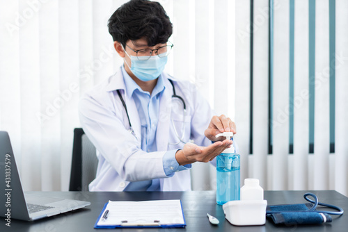 Medical concept a male doctor wearing mask and using hand sanitizer alcohol gel for preventing against infection of Coronavirus  Covid-19  outbreak at his modern clinic