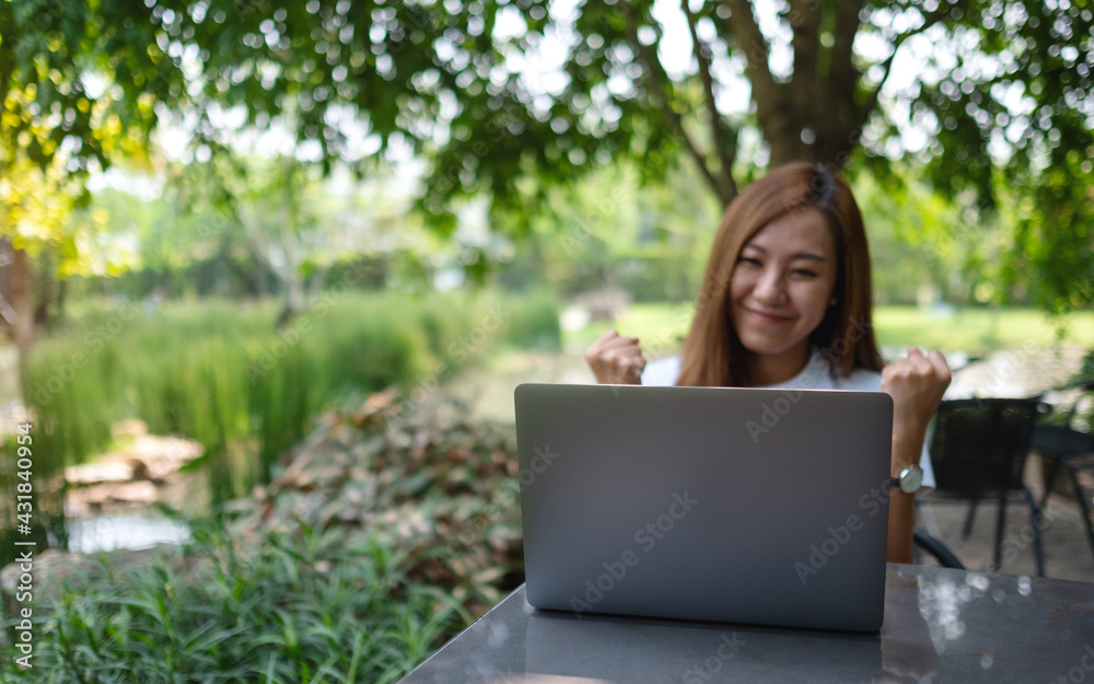 A young asian woman celebrating success while working on laptop computer in the outdoors A young asian woman celebrating success while working on laptop computer in the outdoors