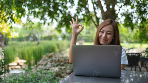 A young asian woman making and showing ok hand sign while working on laptop computer in the park © Farknot Architect