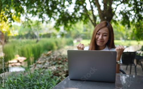 A young asian woman celebrating success while working on laptop computer in the outdoors