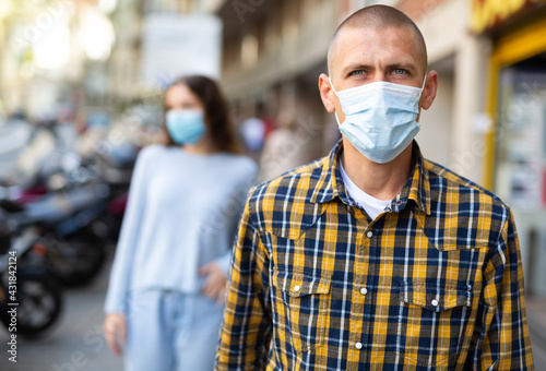 Portrait of young confident man in protective face mask posing on the street