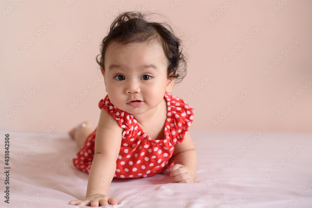 Little Asian baby, a cute toddler dressed in red practicing crawling on the bed and looking at the camera Little Asian baby, a cute toddler dressed in red practicing crawling on the bed and looking at the camera