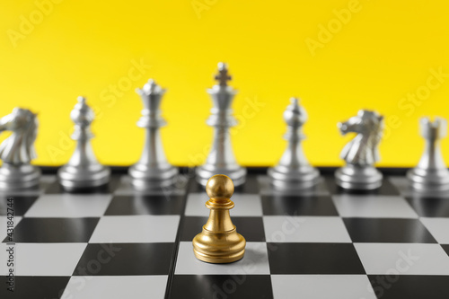 Golden pawn standing out from silver chess pieces on color background