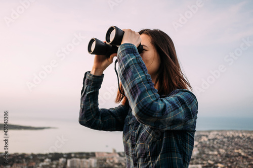 Portrait of a young female tourist looking through binoculars at sunset. photo