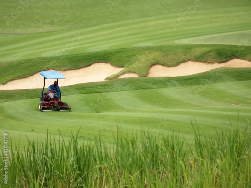Isolated close-up of a Golf course worker using a ride on lawn mower cuts the grass on the fairway in a pattern of lines on an immaculately prepared fairway