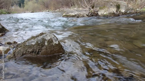 A clear stream of water flows between the stones in the mountains. A fast-moving stream of the river in the mountains