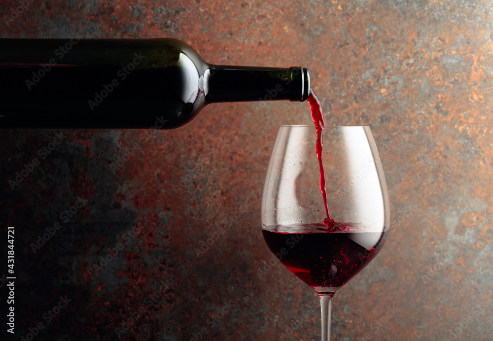 Red wine is poured from a bottle into a wine glass on rusty brown background. - obrazy, fototapety, plakaty 