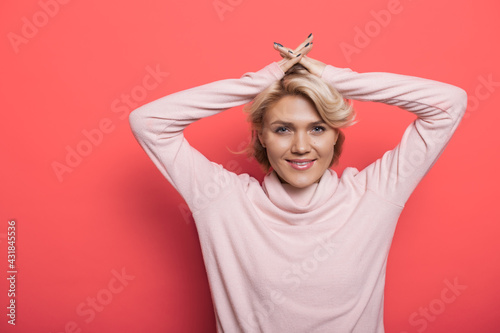 Fotografi Charming blonde woman on a red studio wall is smiling at camera holding hands on