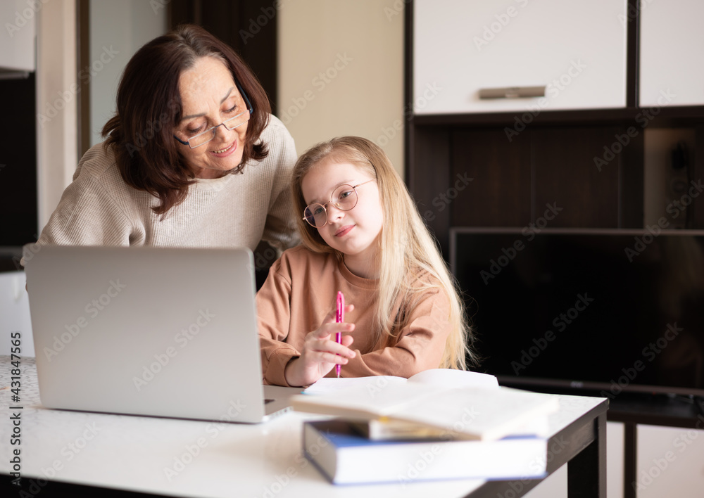Beautiful 10-year-old girl doing homework on a laptop with the support of her grandma. Beautiful 10-year-old girl doing homework on a laptop with the support of her grandma.