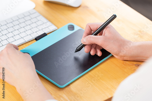 Close-up of female hands using digital graphics tablet and stylus while working in modern office