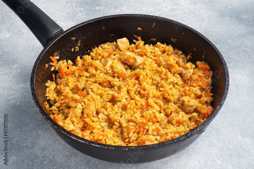 Delicious Asian pilaf, stewed rice with vegetables and chicken in a frying pan. gray concrete background. copy space.
