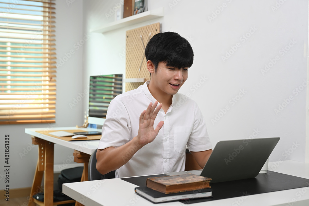 Young man having video call on laptop computer while sitting in home office.