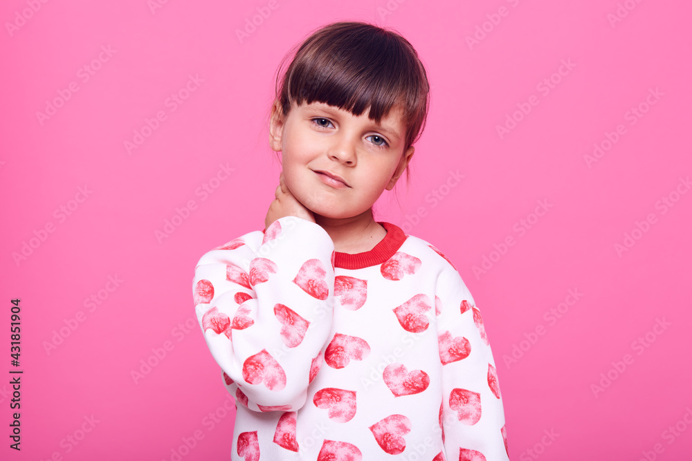 Little charming female kid with dark hair suffering from pain, looking at camera with frowning face, keeping hands on her neck, feels bad, isolated over pink background. Little charming female kid with dark hair suffering from pain, looking at camera with frowning face, keeping hands on her neck, feels bad, isolated over pink background.