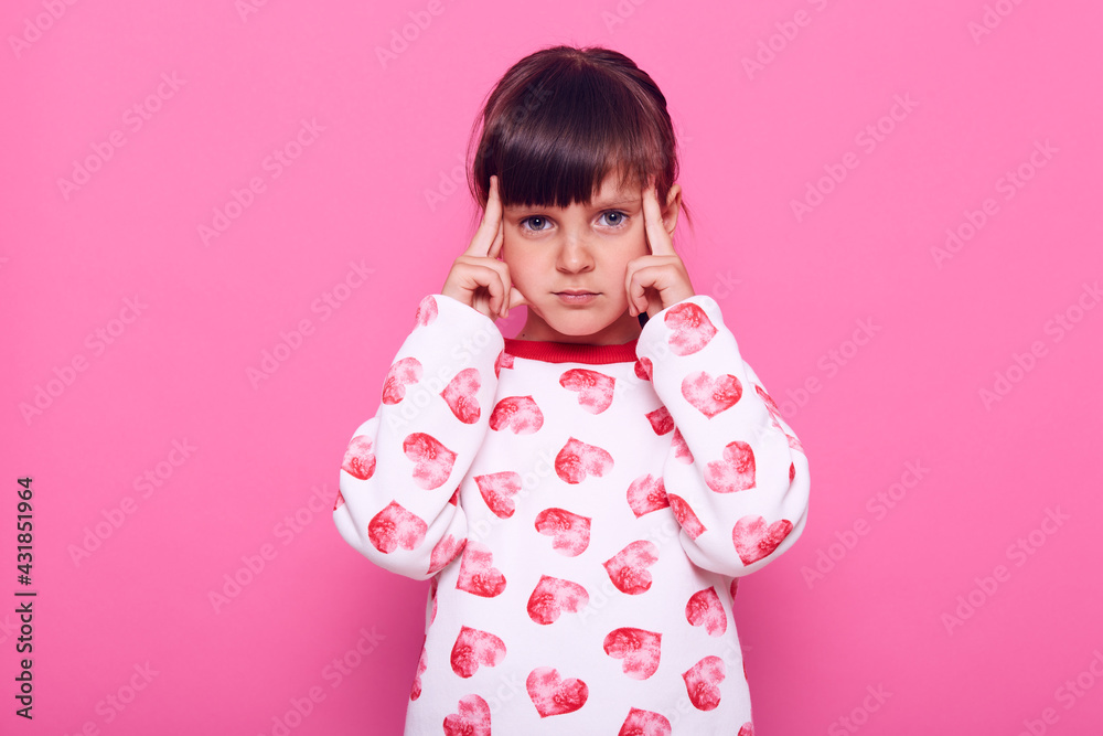 Pensive little cute girl looking at camera, thinks about important things, keeping fingers near temples, being thoughtful and concentrated, isolated over pink background. Pensive little cute girl looking at camera, thinks about important things, keeping fingers near temples, being thoughtful and concentrated, isolated over pink background.