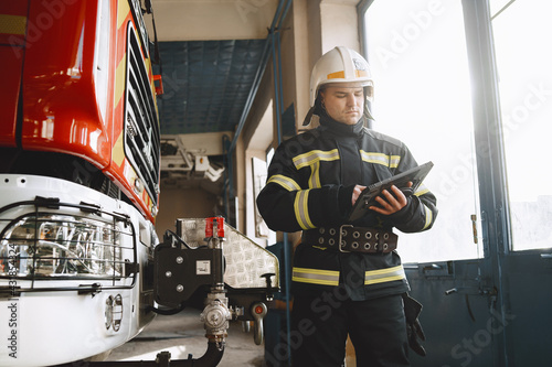 Male firefighter with tablet in uniform on car background photo