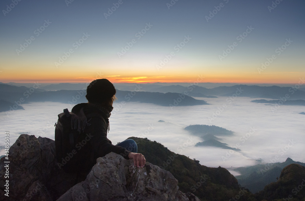 Man sitting on mountain top and contemplating the sunrise, Doi phamon, ChiangRai, Thailand.