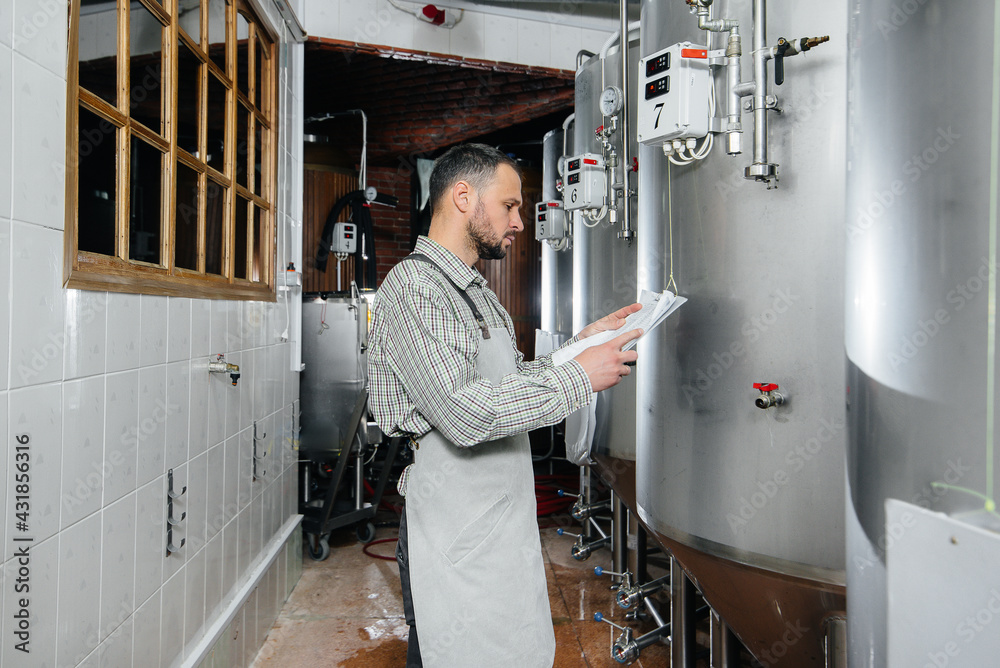 A young bearded brewer monitors the sensor readings during the brewing process. Making beer. A young bearded brewer monitors the sensor readings during the brewing process. Making beer.