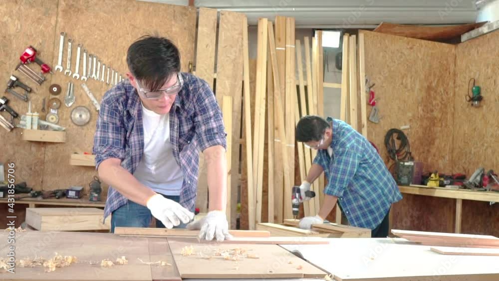 Carpenter in work clothes and small buiness owner working in woodwork workshop. A carpenter is cutting wood in the studio using a chainsaw. Carpenter in work clothes and small buiness owner working in woodwork workshop. A carpenter is cutting wood in the studio using a chainsaw.