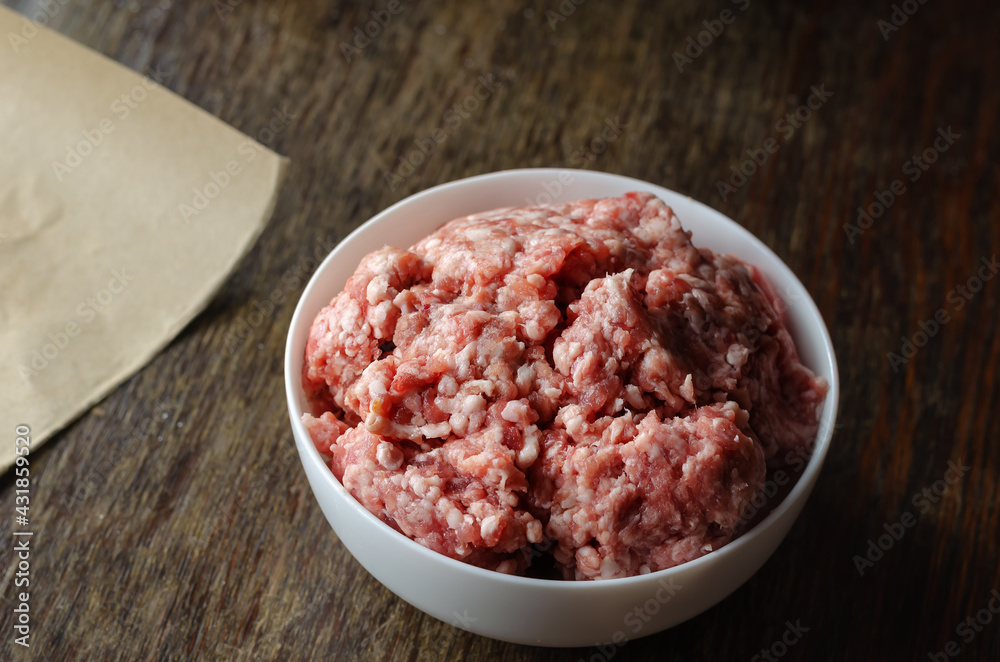 White ceramic bowl with raw minced meat on a dark wooden table. White ceramic bowl with raw minced meat on a dark wooden table.