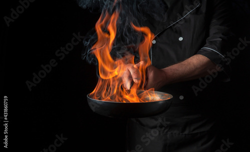 Obraz na plátně Chef cooking food in pan with fire flame on black background
