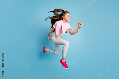 Fototapeta Naklejka Na Ścianę i Meble -  Photo of charming purposeful small schoolgirl dressed t-shirt running fast jumping looking empty space isolated blue color background