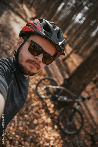 Selfie of a bearded man in cycling helmet wearing sunglasses. A portrait of adventurer with his bicycle behind