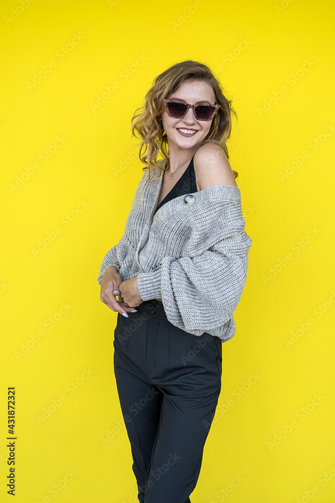 female model posing in gray knitted sweater in sunglasses near yellow wall female model posing in gray knitted sweater in sunglasses near yellow wall