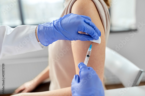 health, medicine and pandemic concept - close up of female doctor or nurse wearing protective medical gloves with syringe vaccinating patient at hospital