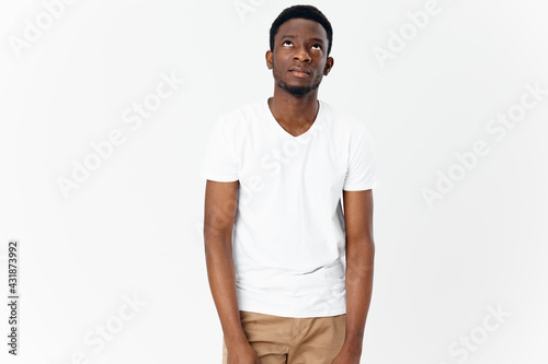 happy african man in white t-shirt and beige pants on light background