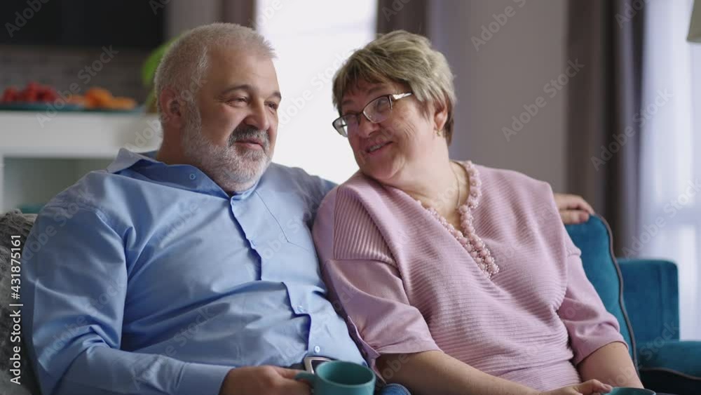cheerful mature man and woman are sitting on couch in apartment and communicating cheerfully, drinking tea and remembering cheerful mature man and woman are sitting on couch in apartment and communicating cheerfully, drinking tea and remembering