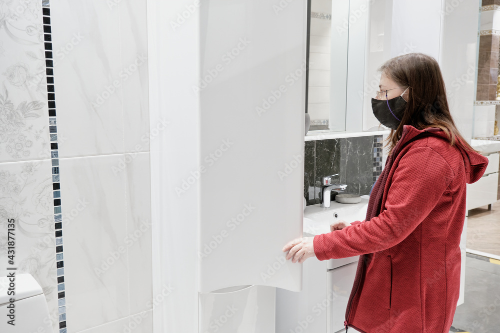 Woman chooses a new kitchen for the house. She wears a mask against the virus. Concept of repair, arrangement of apartment and purchase of new furniture for house Woman chooses a new kitchen for the house. She wears a mask against the virus. Concept of repair, arrangement of apartment and purchase of new furniture for house