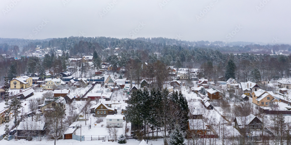 Winter rural landscape. Aerial view of a snow-covered village. Top view of the streets, houses and trees. Cold snowy winter weather. Snowfall. Snow on the roofs. Toksovo, Leningrad region, Russia.