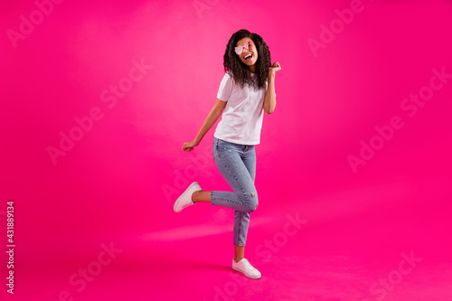 Full size photo of funny young lady dance wear spectacles t-shirt jeans sneakers isolated on pink color background © deagreez