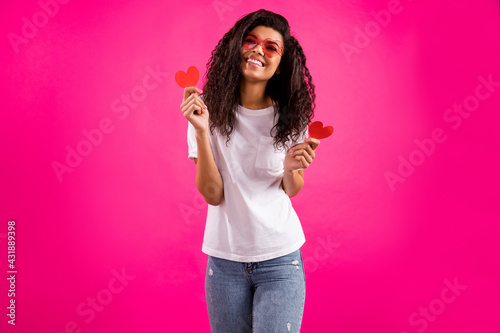 Photo of romantic young lady hold hearts wear spectacles t-shirt jeans isolated on pink color background