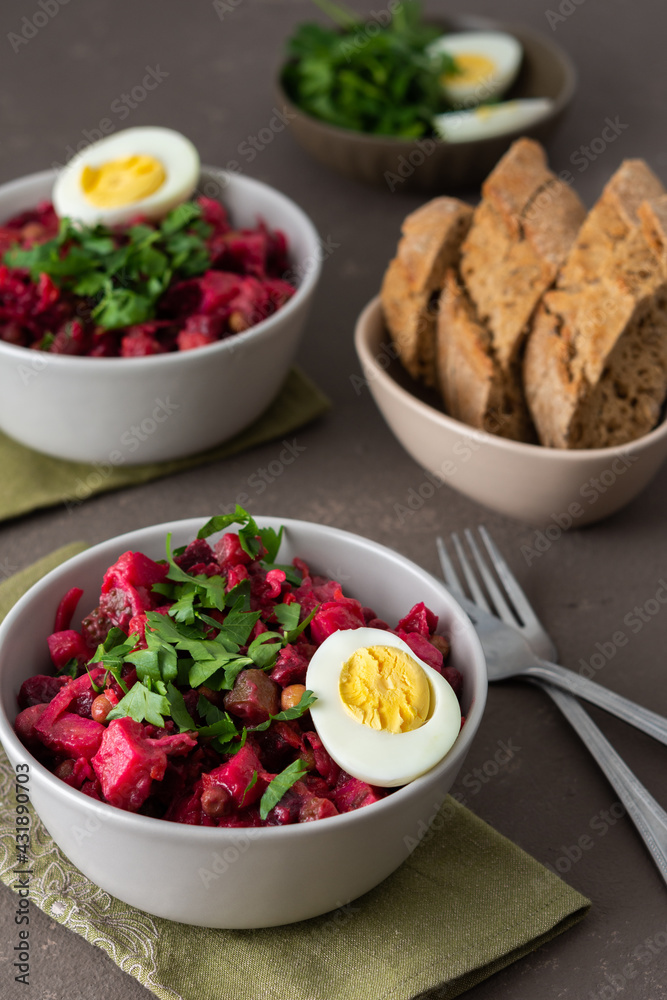Russian salad vinaigrette in plates with boiled egg and black bread, salad of boiled potatoes and carrots, beetroot and pickled vegetables, cucumber and cabbage and canned green peas