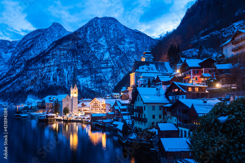 Hallstatt Cityscape on a Cold Winter Evening Covered with Snow with the Lake Hallstaetter See and Church Illuminated at Night