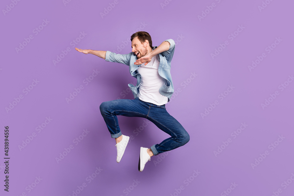 Photo of pretty excited young man wear jeans shirt jumping high looking empty space isolated violet color background