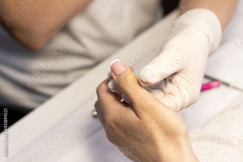 Manicure. Covering natural nails with gel polish, white french coat and nail design in a beauty salon by a manicure master. Close-up