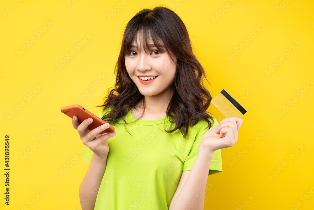 Young girl holding phone and credit card with cheerful expression on background Young girl holding phone and credit card with cheerful expression on background
