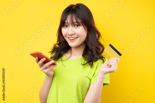 Young girl holding phone and credit card with cheerful expression on background