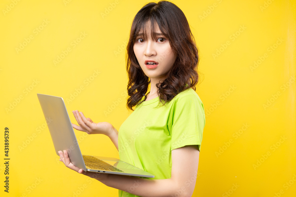 Young asian girl using laptop on yellow background Young asian girl using laptop on yellow background