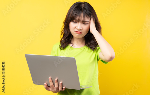 Young asian girl using laptop on yellow background