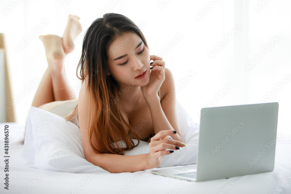 Young Asian female resting on bed and using netbook Young Asian female resting on bed and using netbook